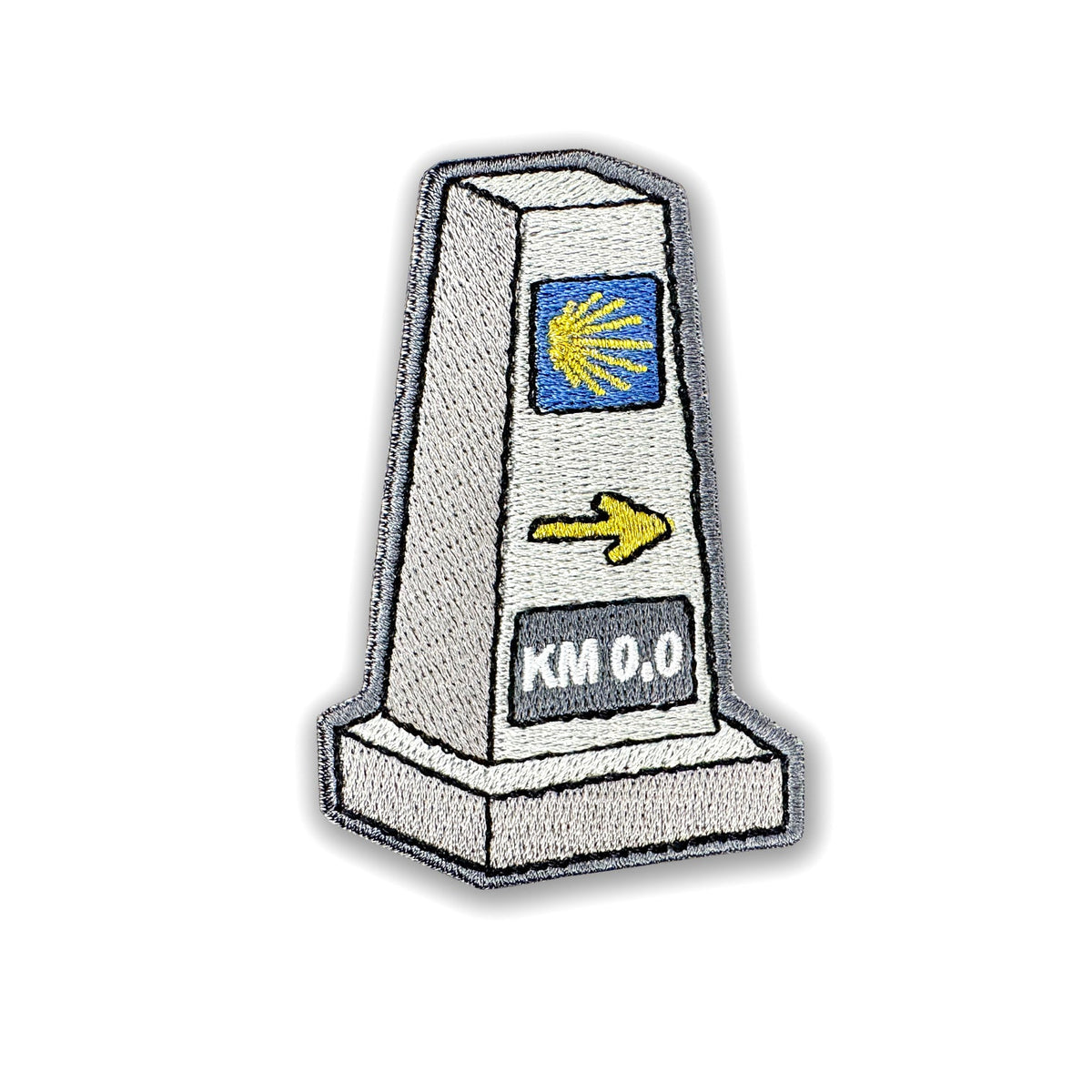 Pilgrim Artifact Camino Mojón Milestone embroidered iron-on patch shaped like a stone waymarker, with a yellow scallop shell on blue, a yellow right-pointing arrow, and KM 0.0 lettering, shown on a white background. 