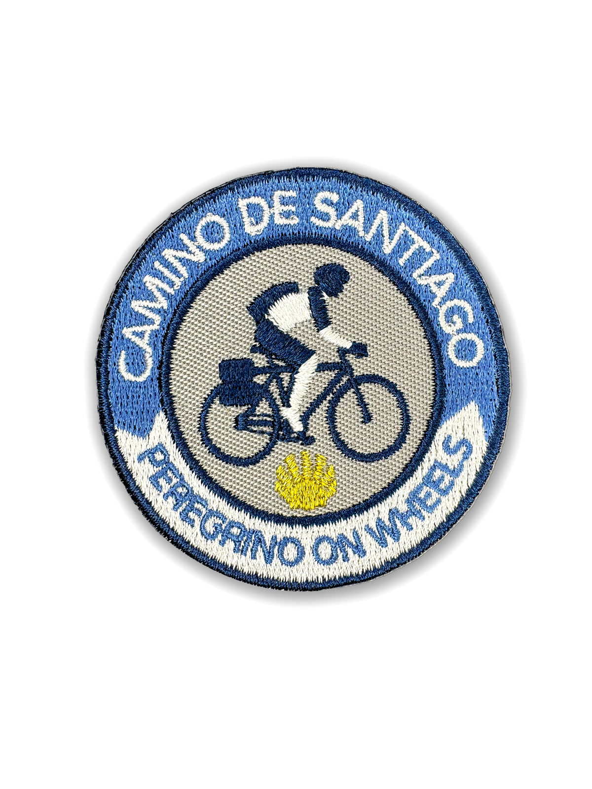 Pilgrim Artifact Peregrino On Wheels embroidered iron-on patch featuring a cyclist on a touring bicycle, a yellow scallop shell, and a blue and white Camino de Santiago border, shown on a white background. 