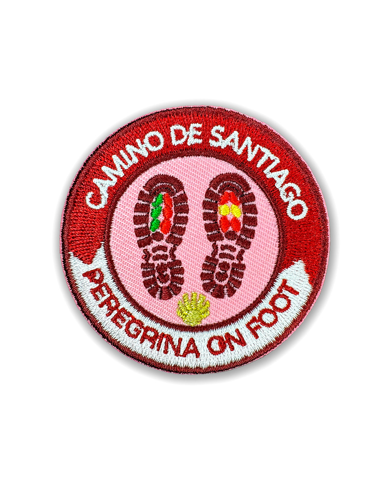 Pilgrim Artifact Peregrina On Foot embroidered iron-on patch with boot prints containing Portuguese and Spanish flag colors on a pink center, a gold scallop shell, and a red and white border, shown on a white background. 